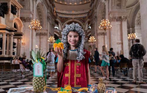 A young boy, dressed as Christopher Wren, holds a pineapple inside the Cathedral