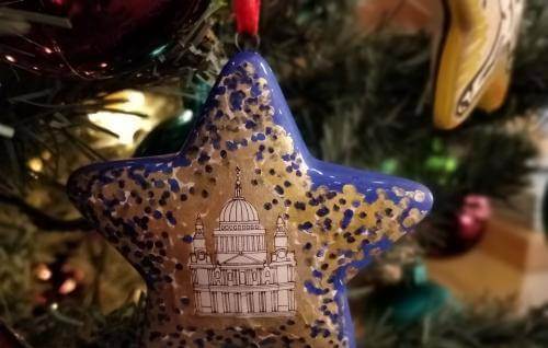 A blue and gold star Christmas decoration hangs from a Christmas tree