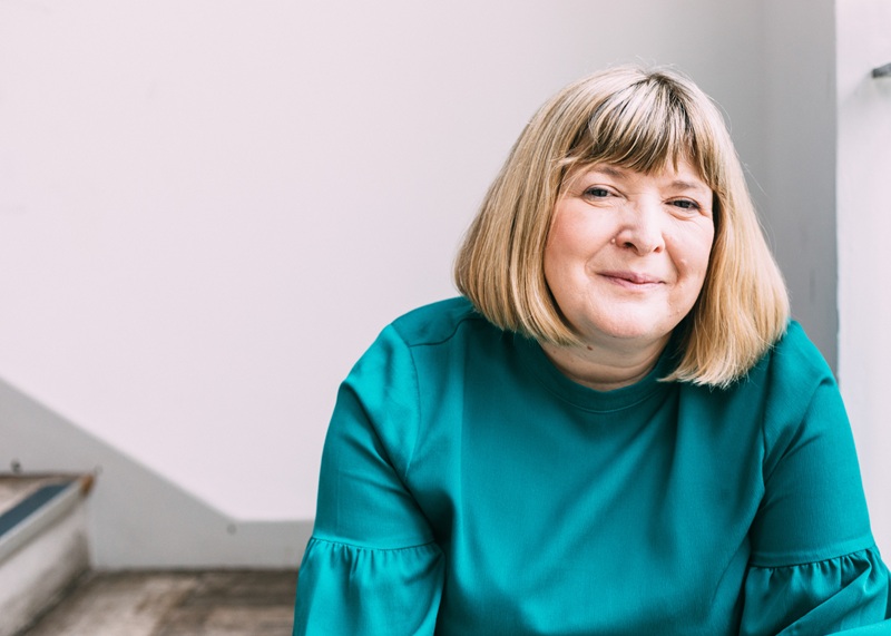A woman with a straight blond shoulder length bob wearing a deep green blouse