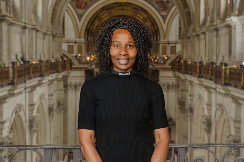 Catherine has curly black hair and wears a clerical collar and a black dress, while standing at the West gallery in St Paul's Cathedral