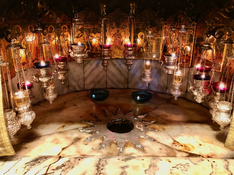A photo of the 14 pointed star which marks the traditional place of Jesus' birth, lit by many golden hanging lamps