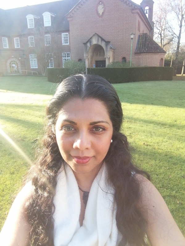 Sanjee has long dark hair and wears a white scarf over a black beaded necklace.