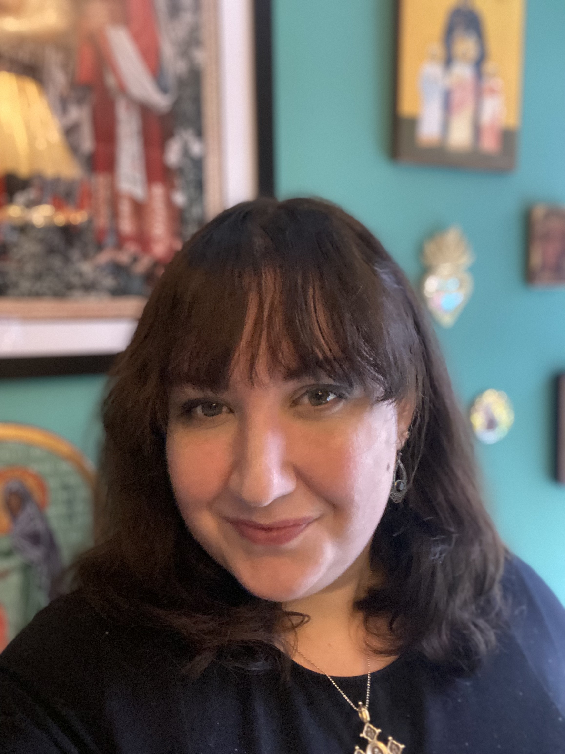 Charlotte has long brown hair, stands in front of a wall decorated with icons