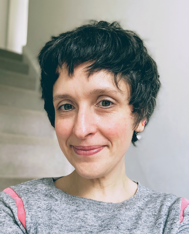 Susie has short dark hair and wears a grey jumper with a pink stripe