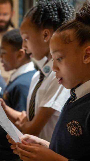 girls and boys in school uniform singing from sheet music