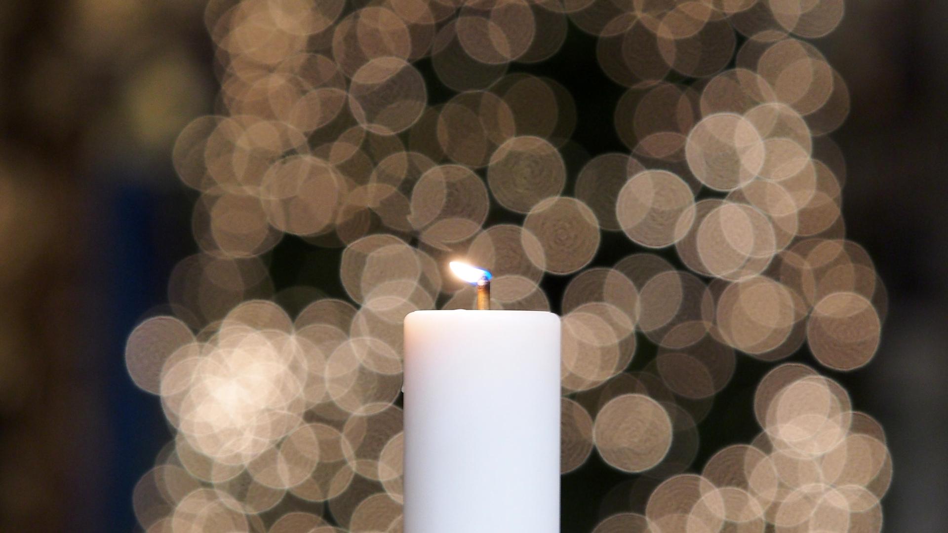 A lit candle with a Cathedral Christmas tree in the background