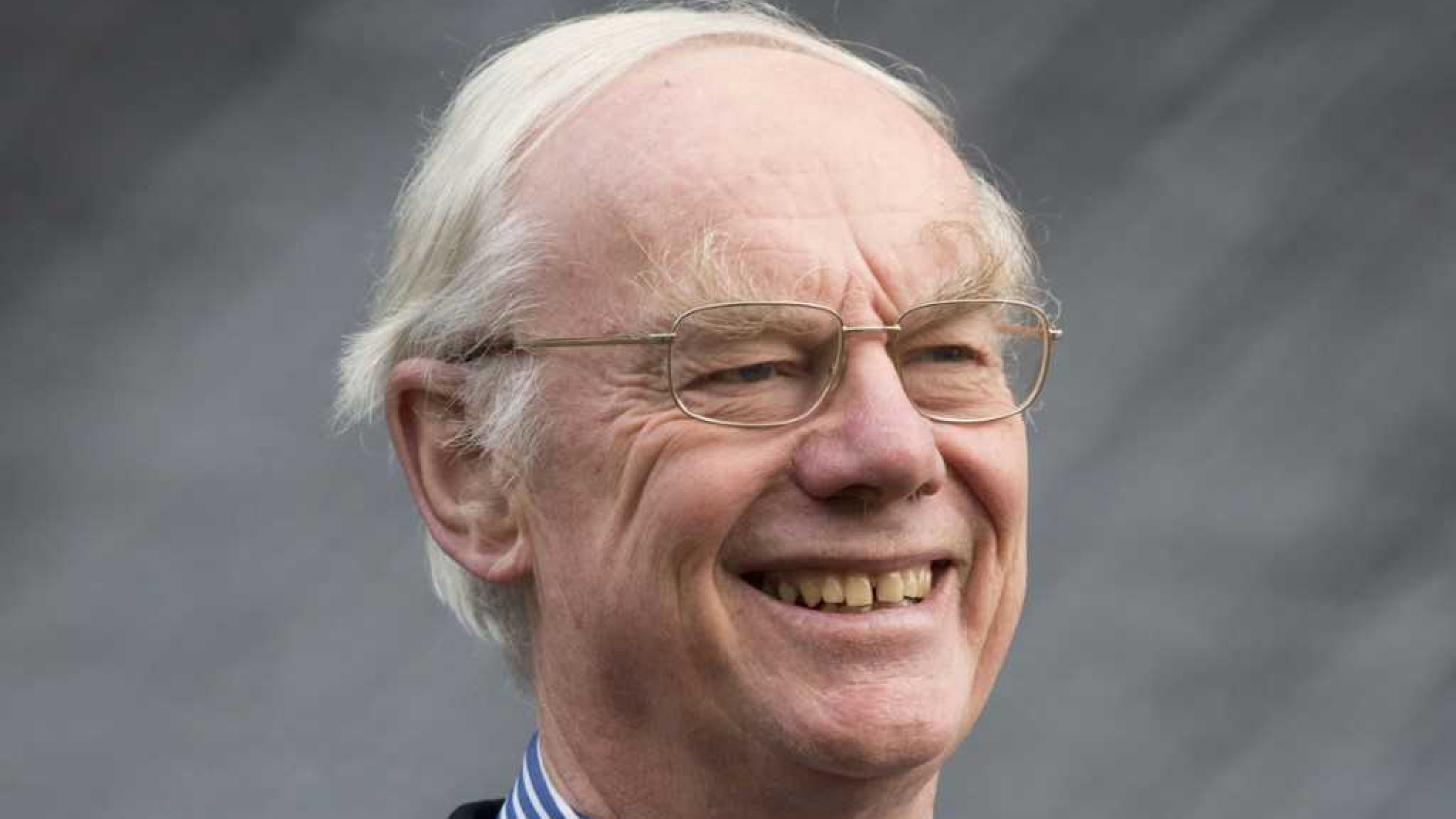 A grey-haired white man with glasses wearing academic robes over a suit and tie.
