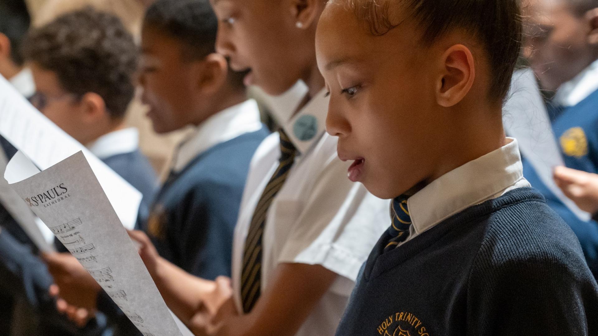 girls and boys in school uniform singing from sheet music