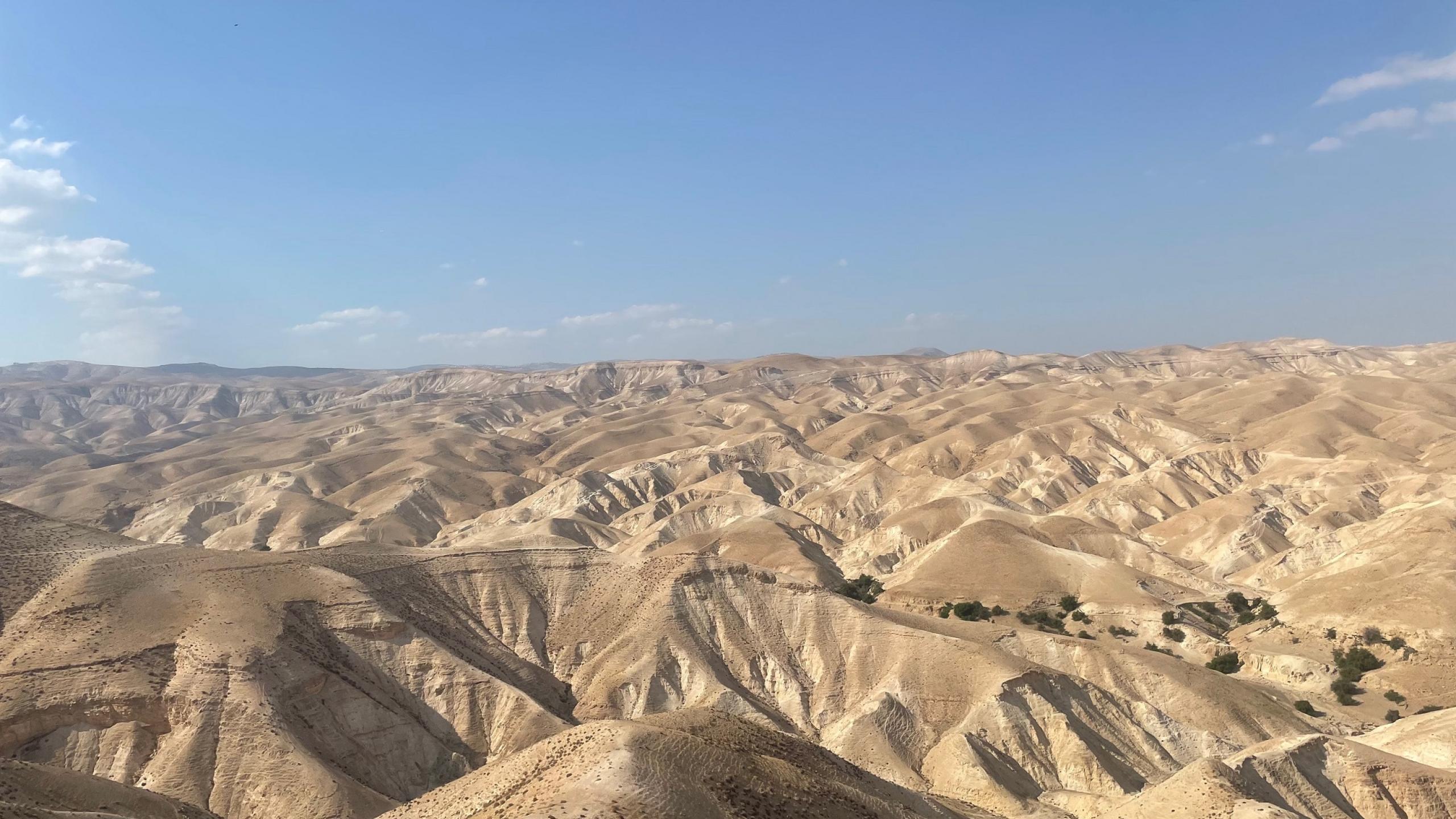 Looking across the ridges of the desert towards the blue sky with a few wispy clouds.