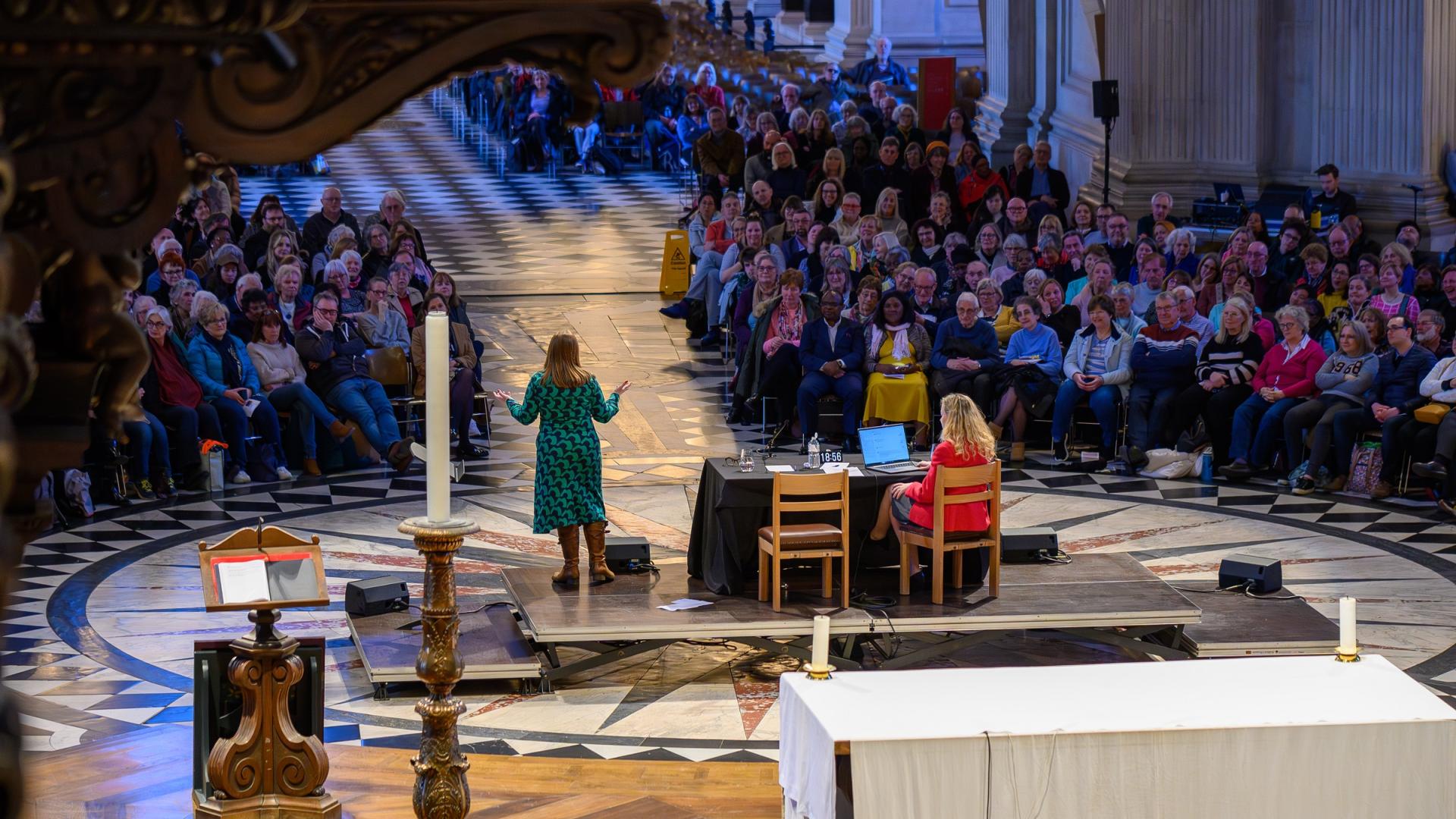 A view of the cathedral with a large audience facing a stage with a speaker in a green dress