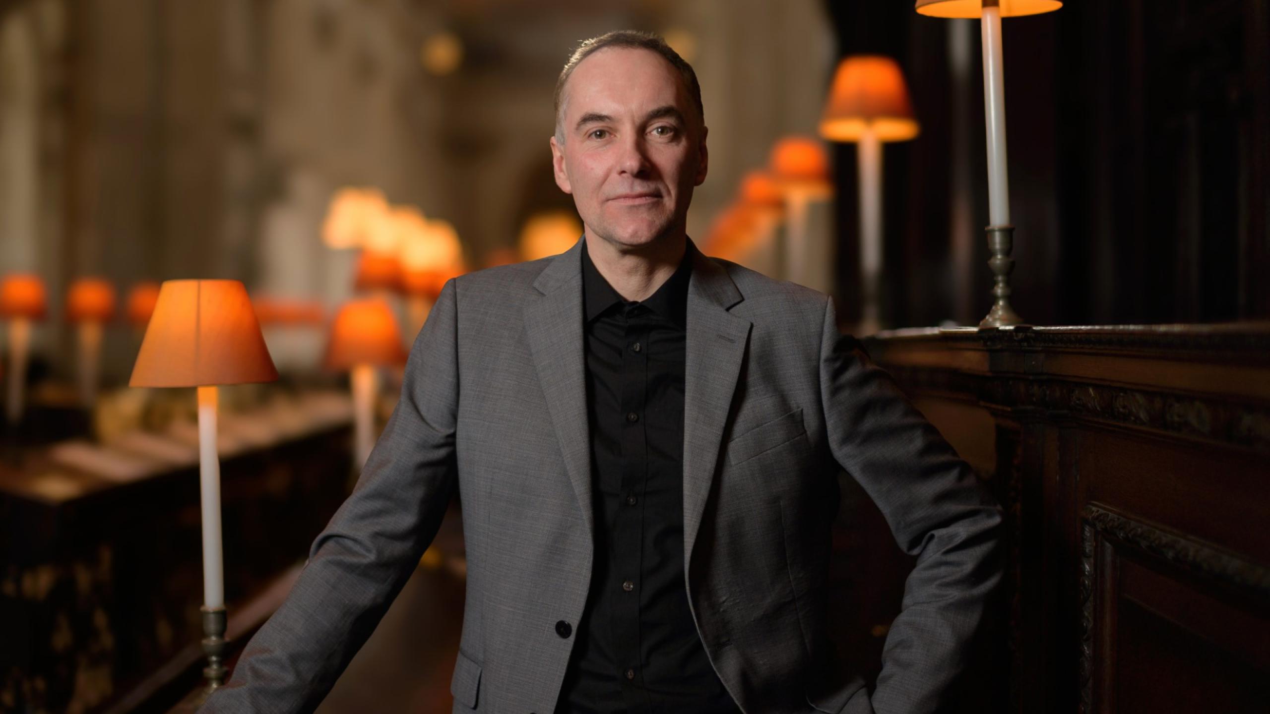 An image of a white man with cropped hair and grey suit jacket standing in front of choir stalls inside St Paul's Cathedral