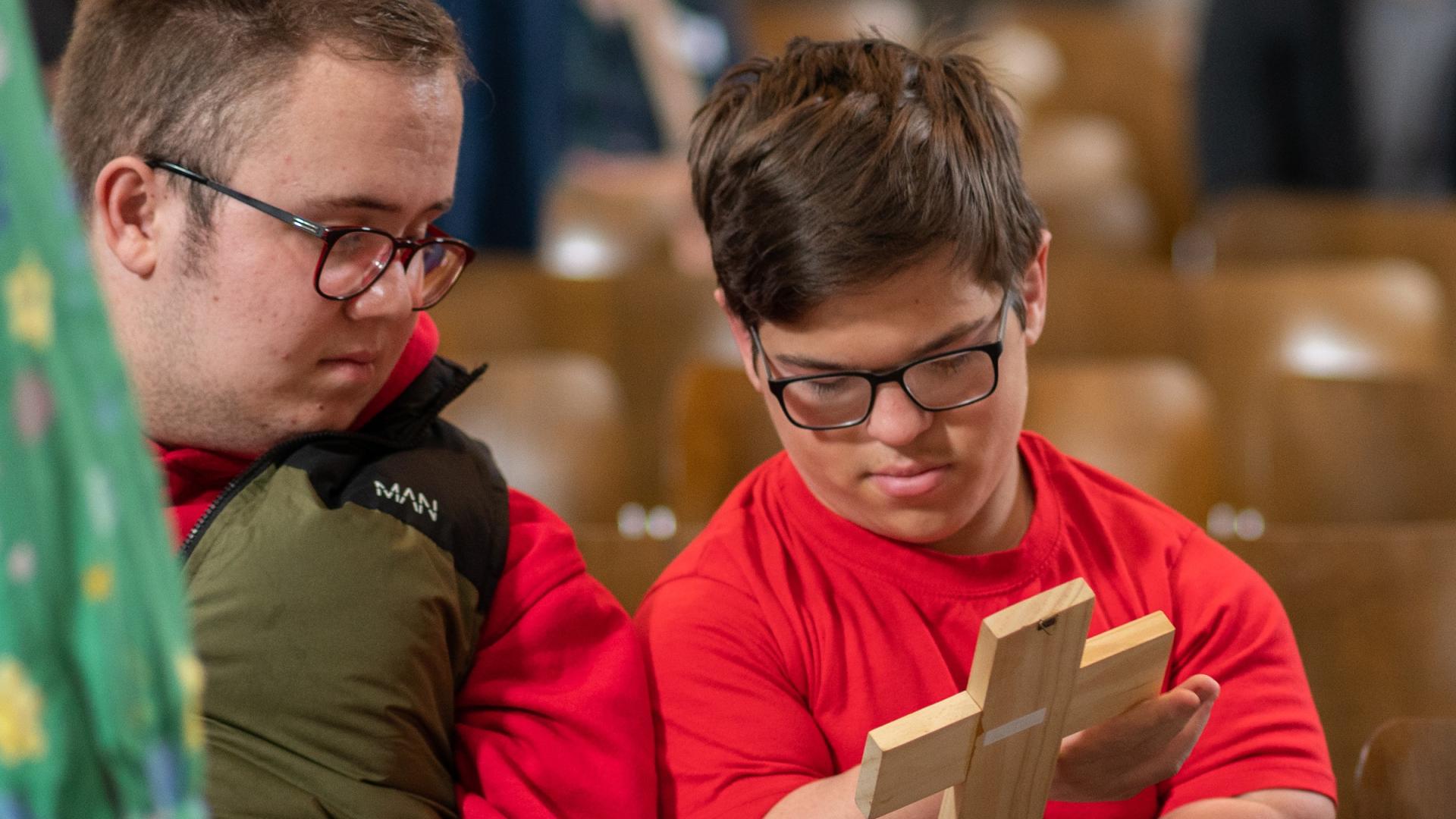 Child handles wooden cross with adult alongside