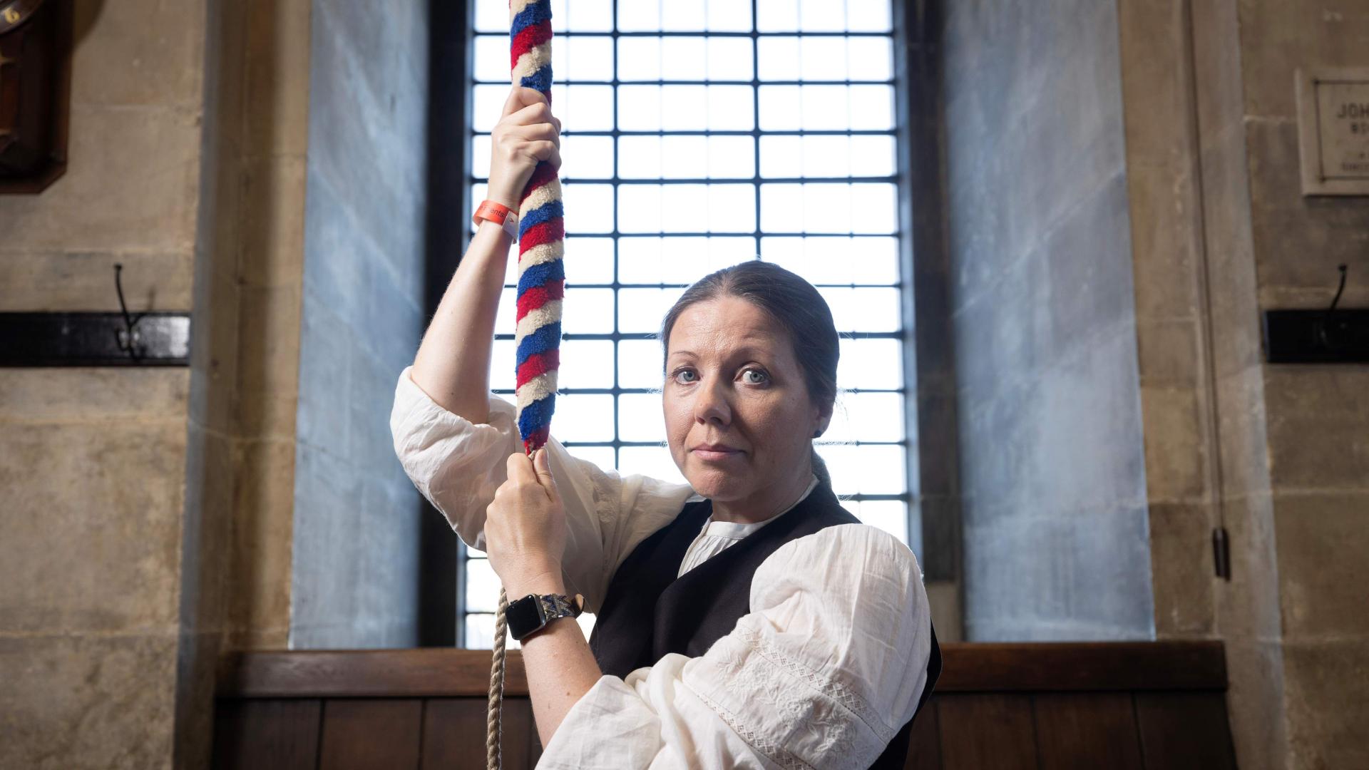 A bereaved mother faces the camera and while pulling a bell rope