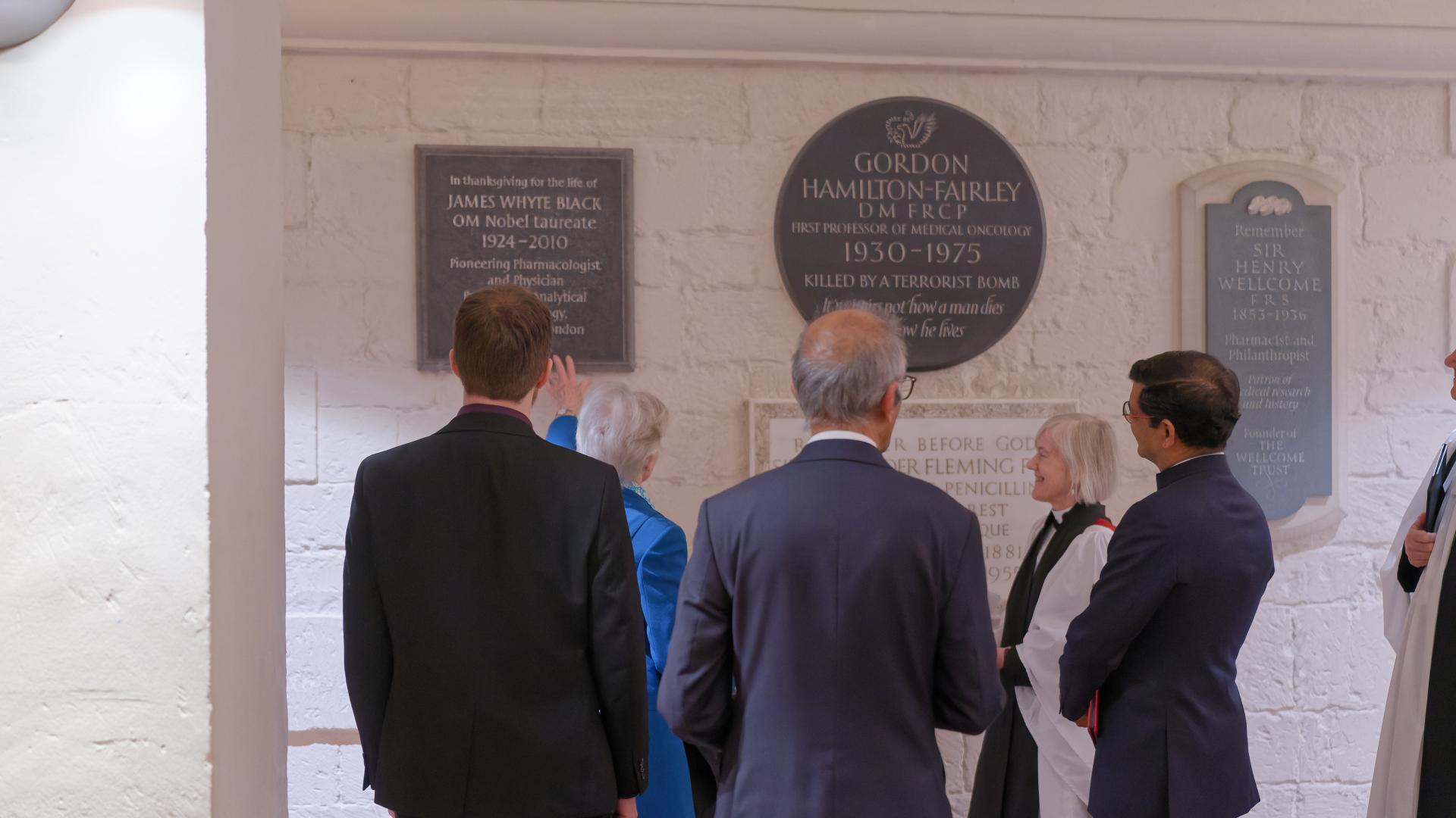 A group of people stand in front of a memorial plaque in the Crypt.