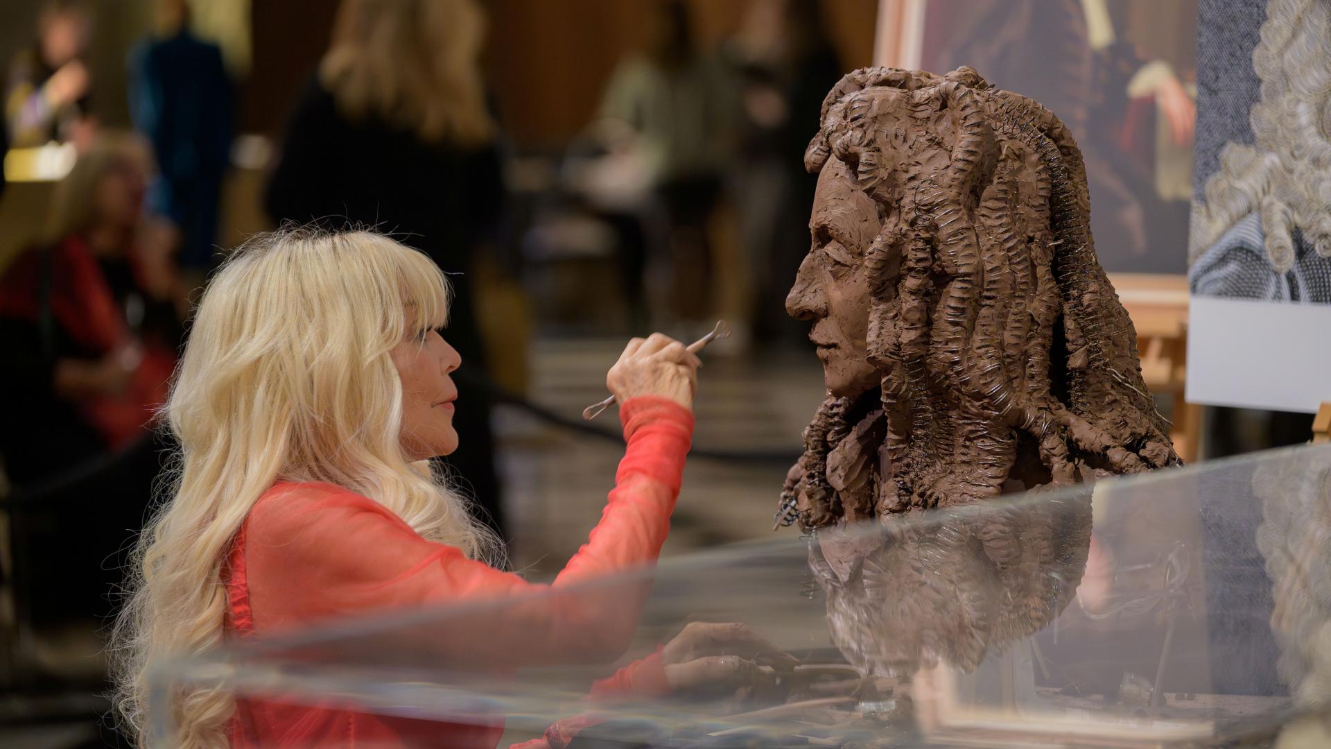 Lady Petchey sculpting a bust of Christopher Wren from dark clay.