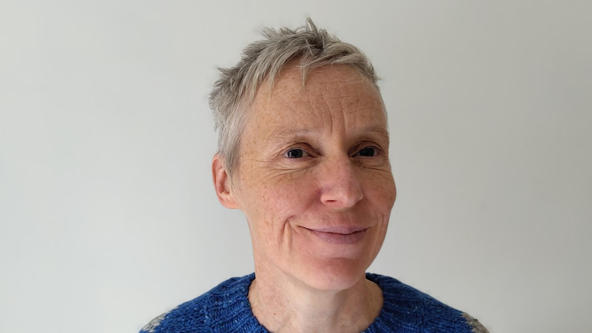 A woman with short grey hair wearing a blue sweater