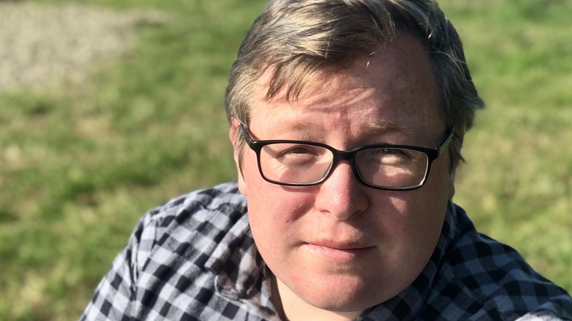 A man with blond hair and glasses wearing a checked shirt