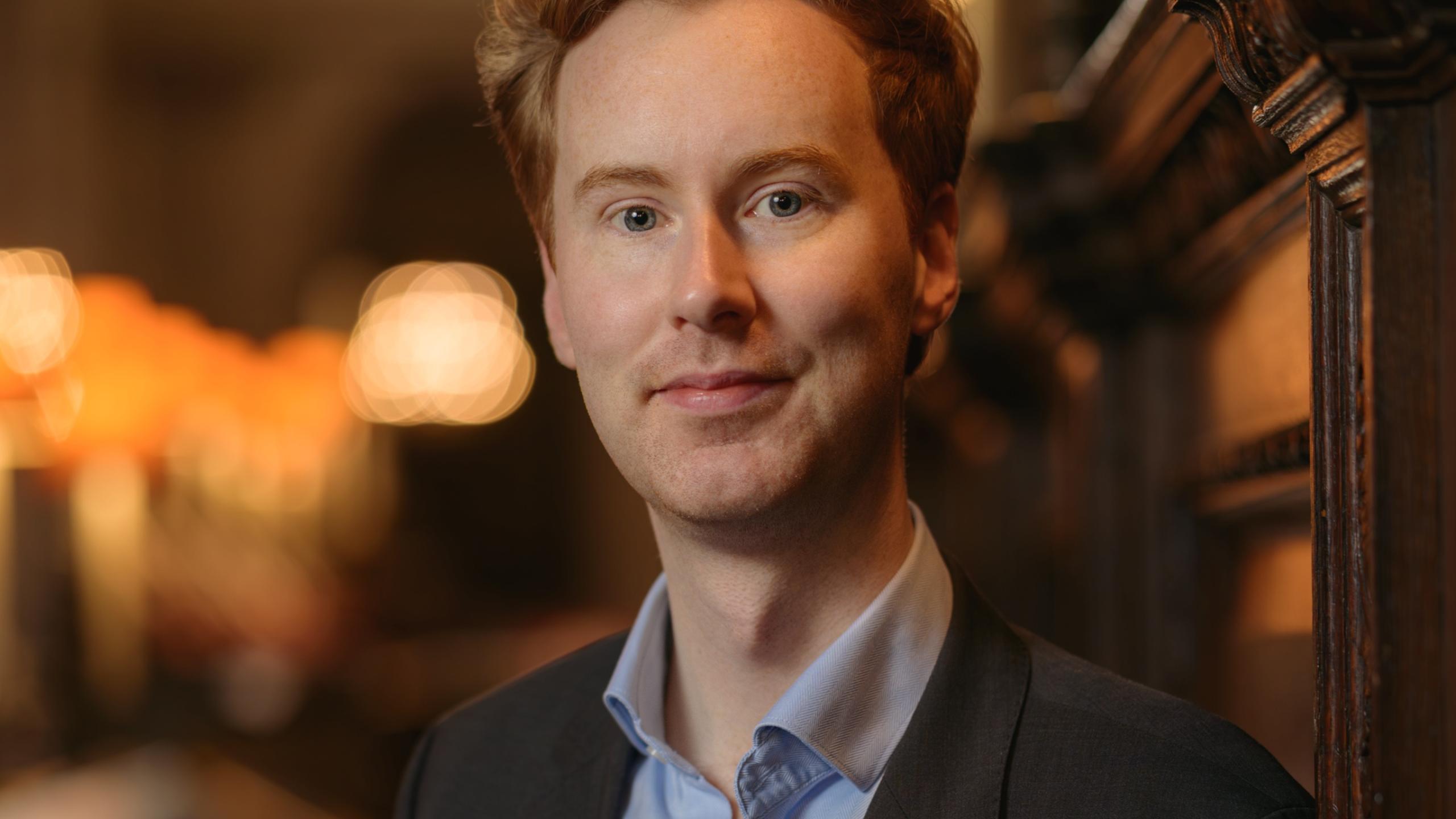 James stands in the quire of St Paul's Cathedral wearing a black jacket over a pale blue shirt