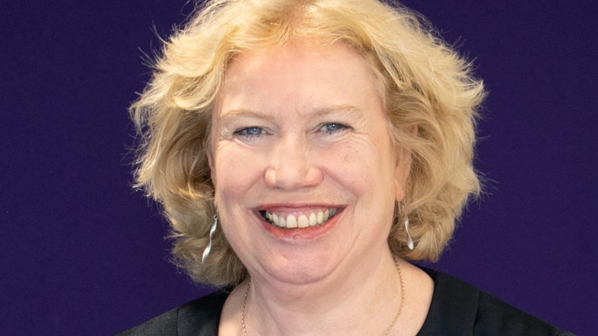 Meg Munn, a white woman with blonde hair, photographed in front of a navy blue background.