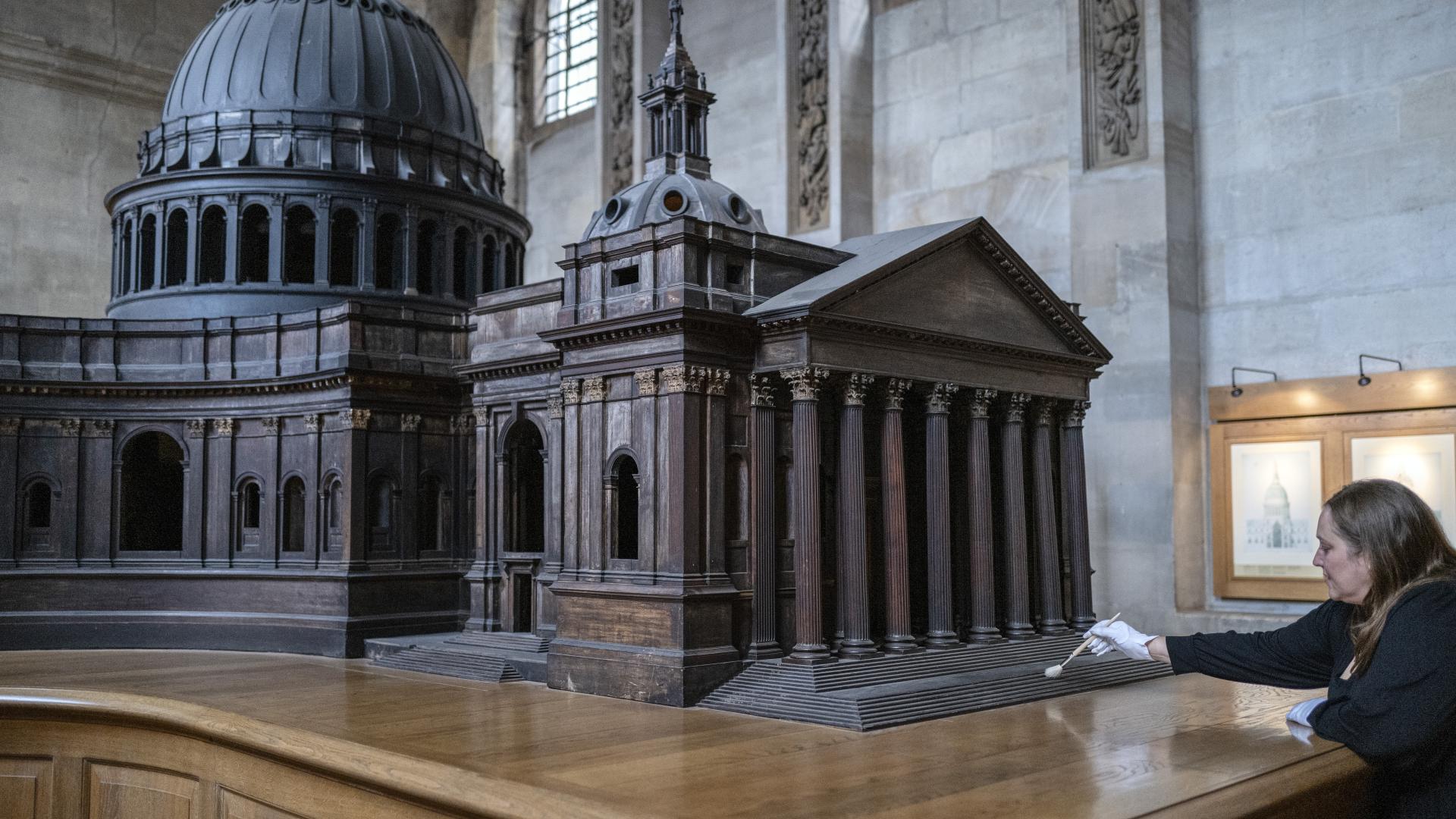 a wooden model of the cathedral made by Christoppher Wren with conservator cleaning the base wearing white gloves