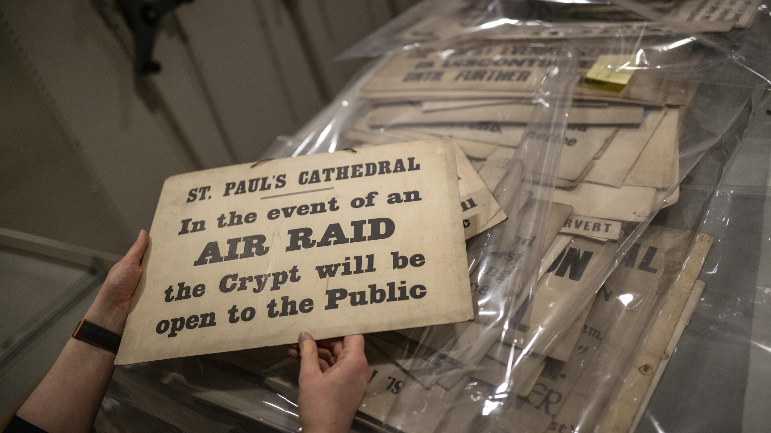 A member of the Collections team handles an old sign which says, 'St Paul's Cathedral: In the event of air raid, the Crypt will be open to the Public'