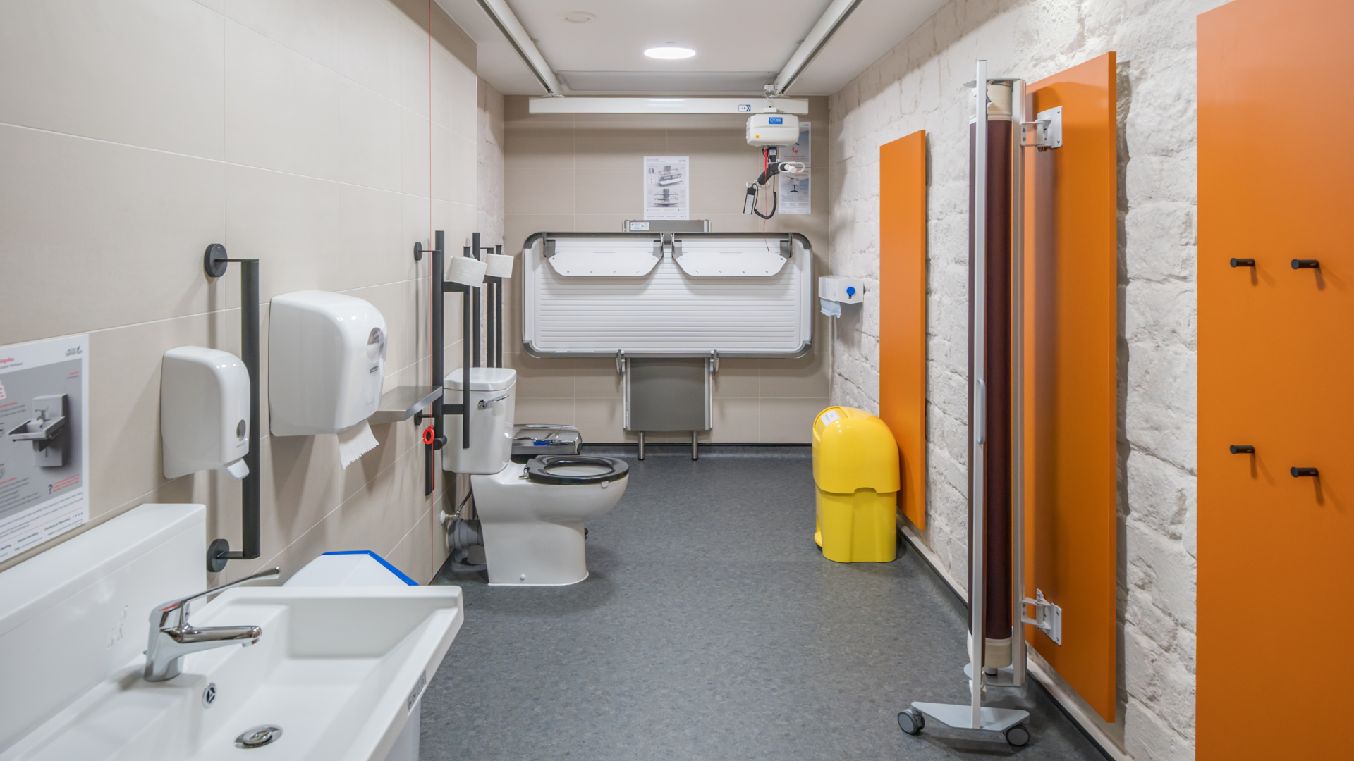 An interior photos of a changing places toilet featuring a height adjustable sink, toilet, hoist and changing table.