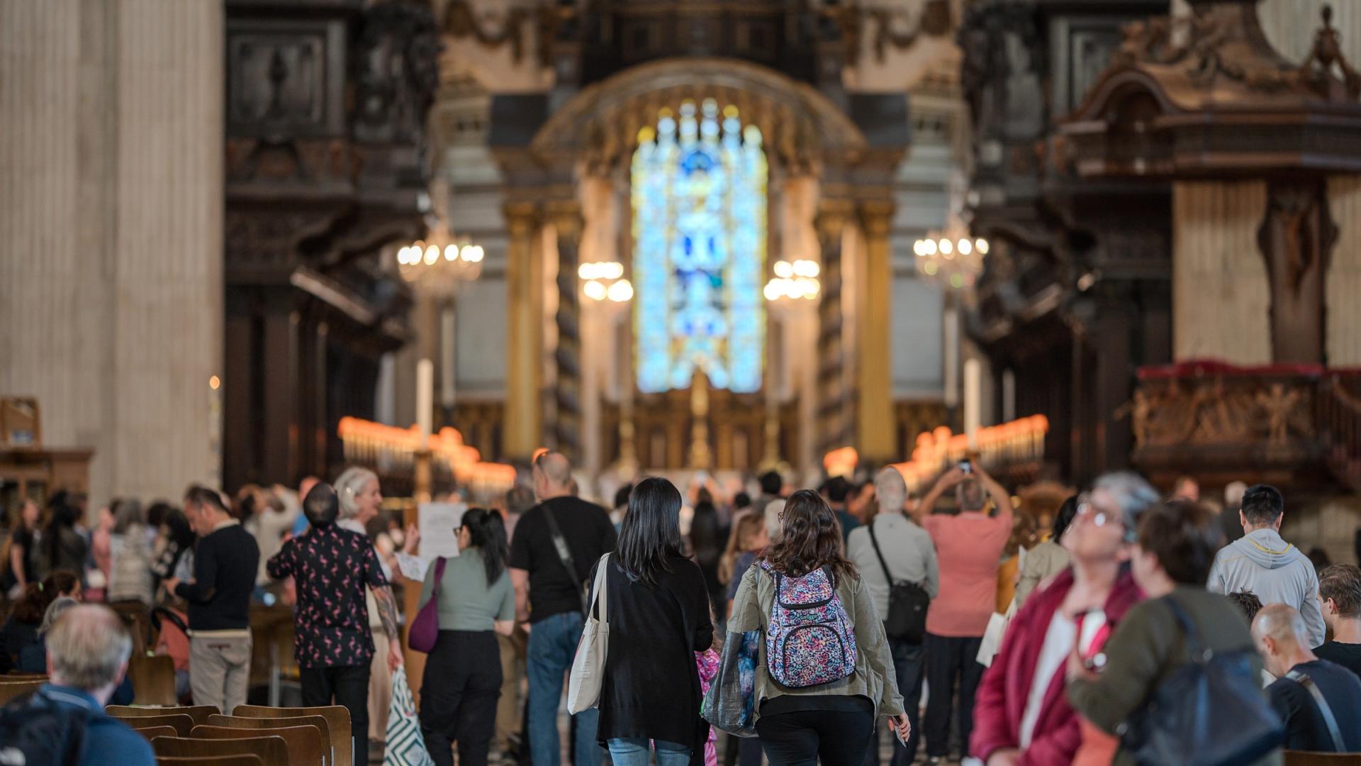 A large number of people wander around the nave of the cathedral, looking around them as they walk