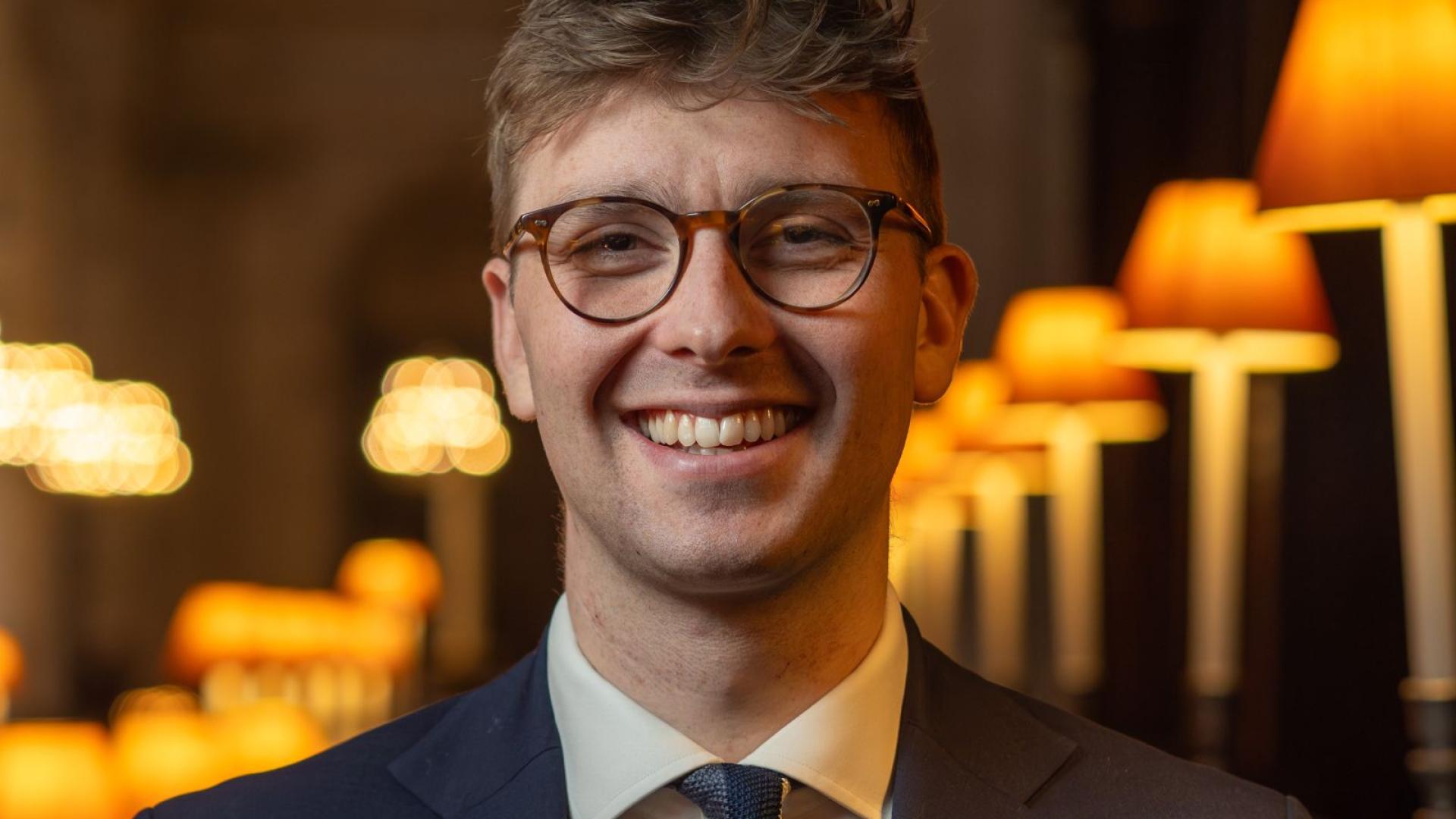 George Cook smiling wearing glasses, a blue suit jacket and a blue striped tie