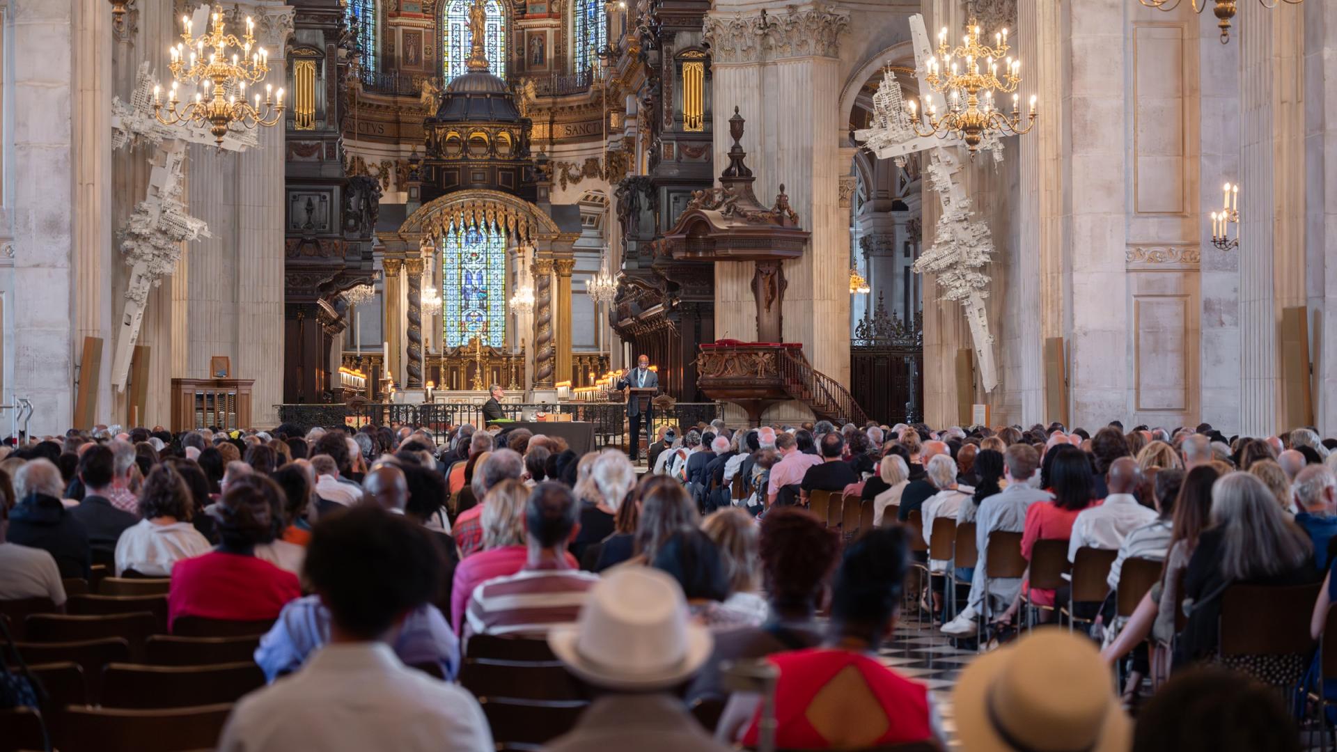 A large audience in the Cathedral watch a man talking from a stage