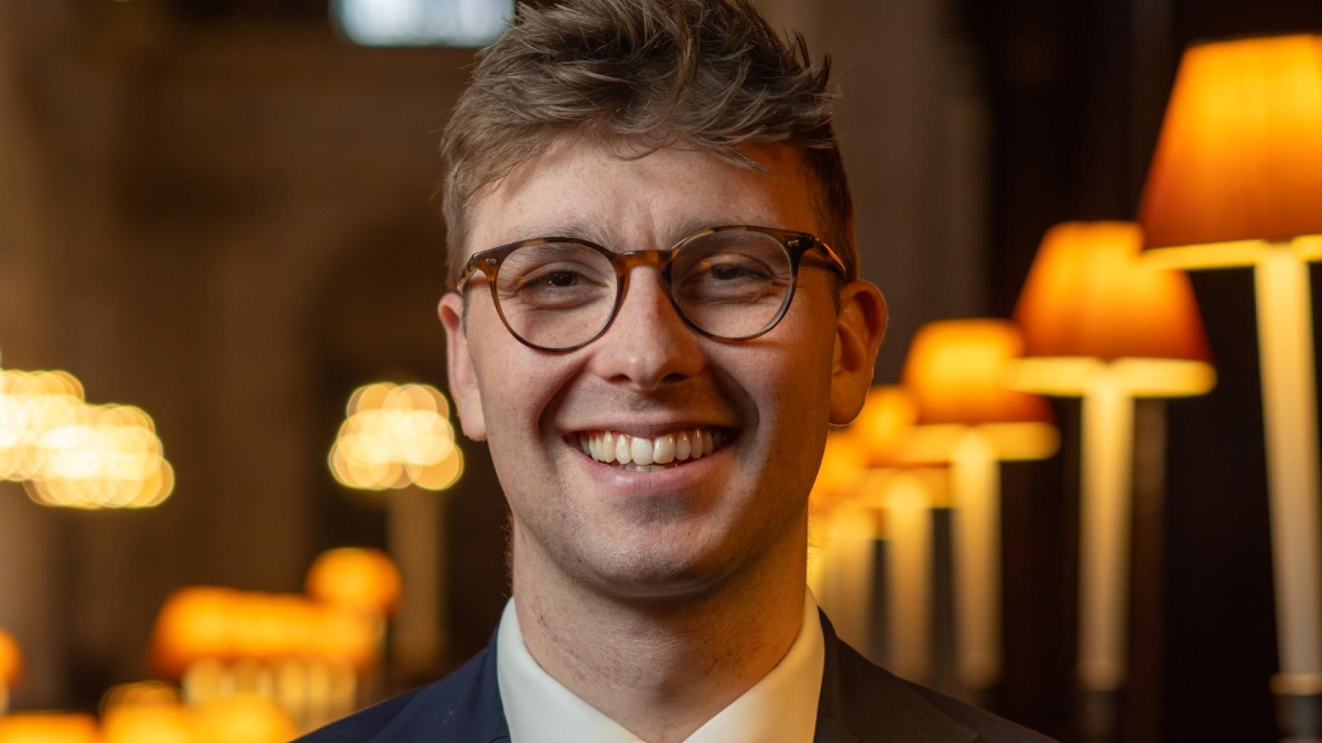 George Cook smiling wearing glasses, a blue suit jacket and a blue striped tie