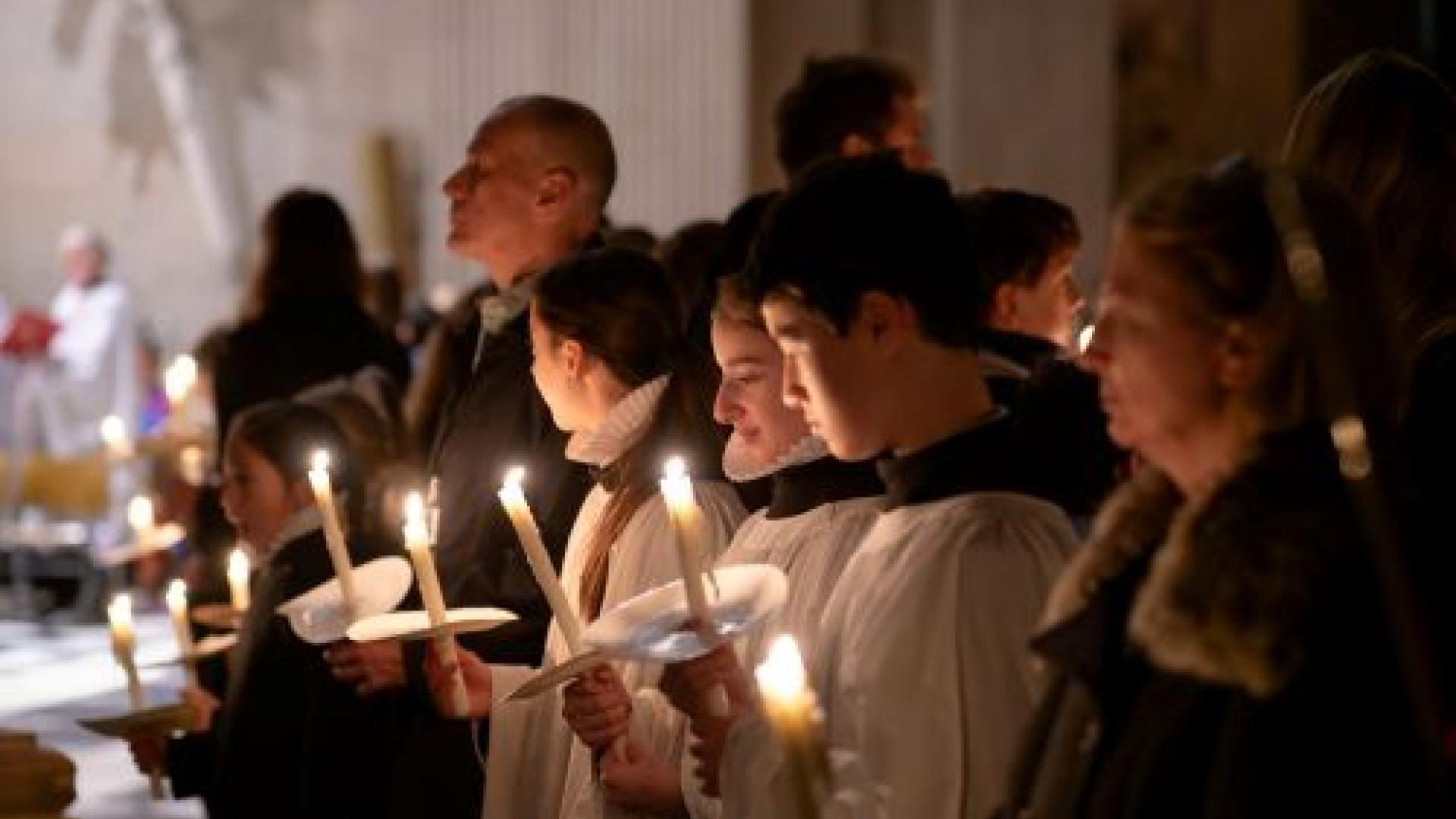 Choristers and adults stand holding lit candles at Advent