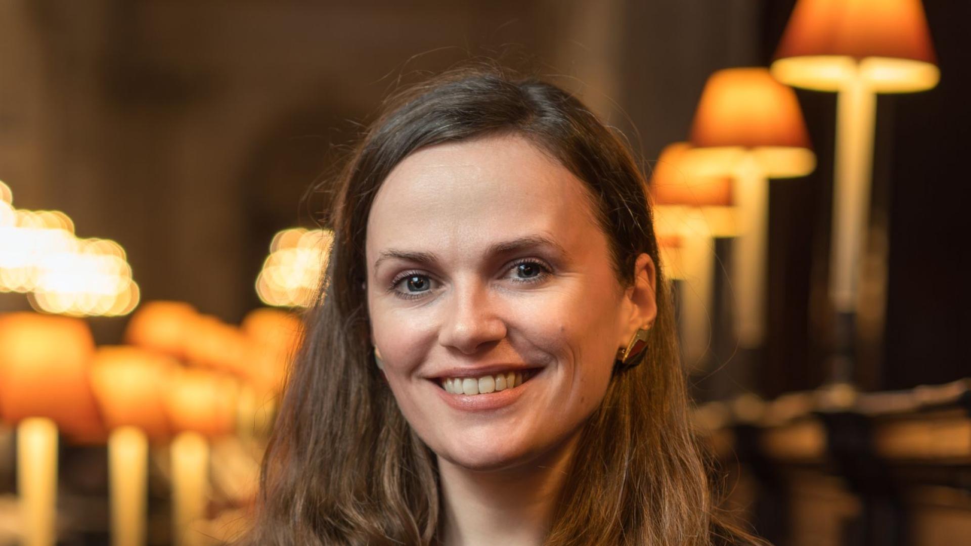 Laurel Lamb smiling with brown wavy hairy, wearing a floral patterned blouse and black jacket
