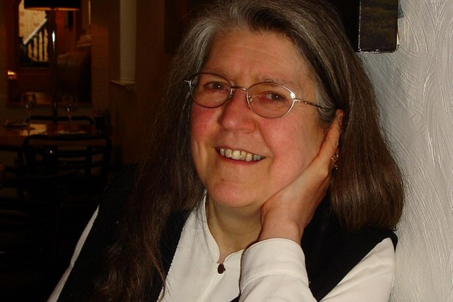 Janet Tollington leans her elbow on a table and with her hand under her chin smiles towards the camera
