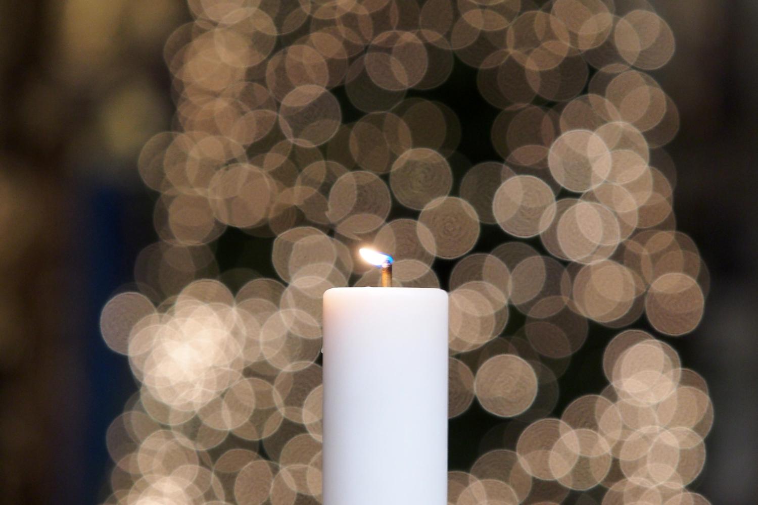 A lit candle with a Cathedral Christmas tree in the background