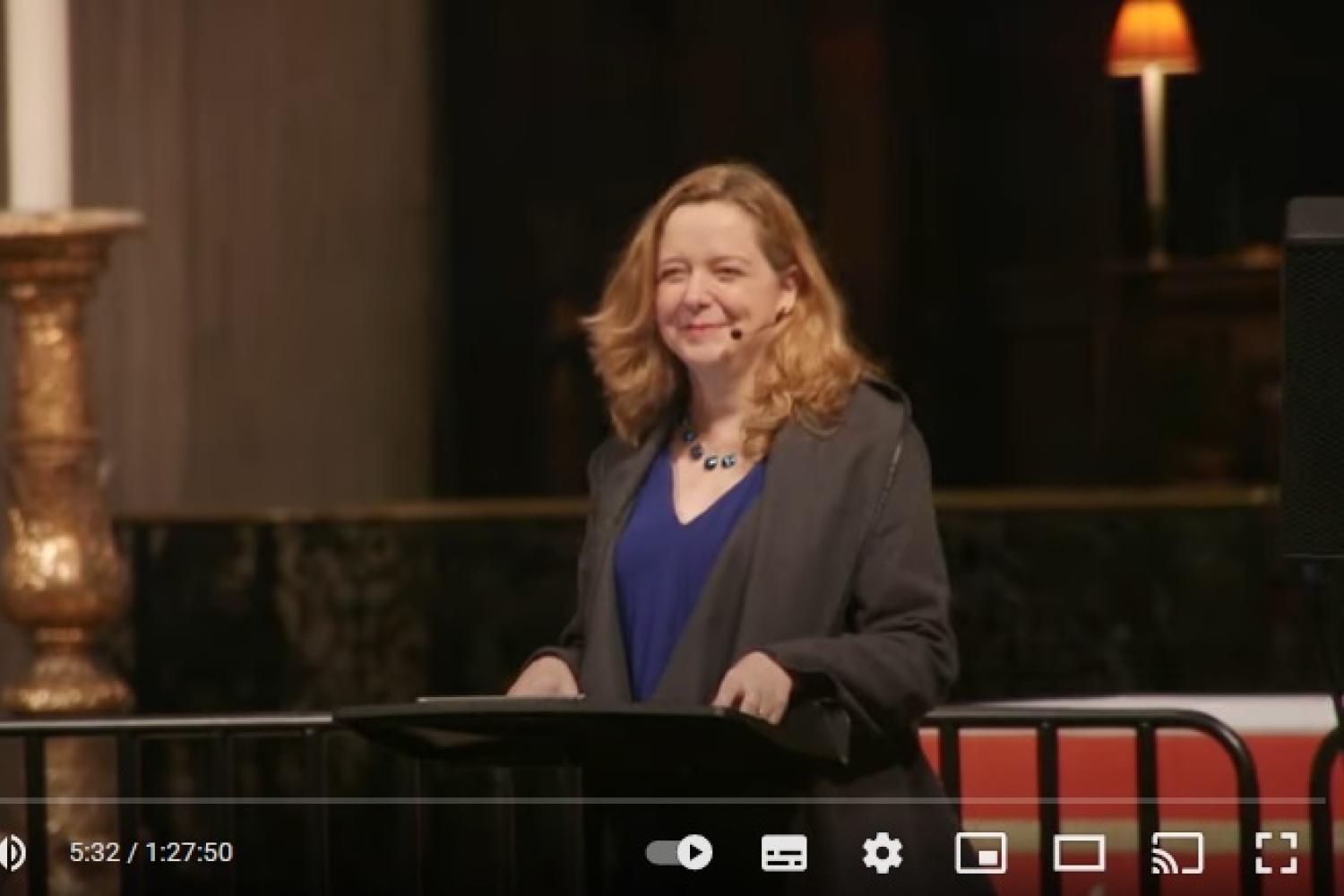 Paula Gooder smiles at the lectern in St Paul's Cathedral. Behind her you can see the front of the quire and one of its lamps and a large white candle on its golden stand.