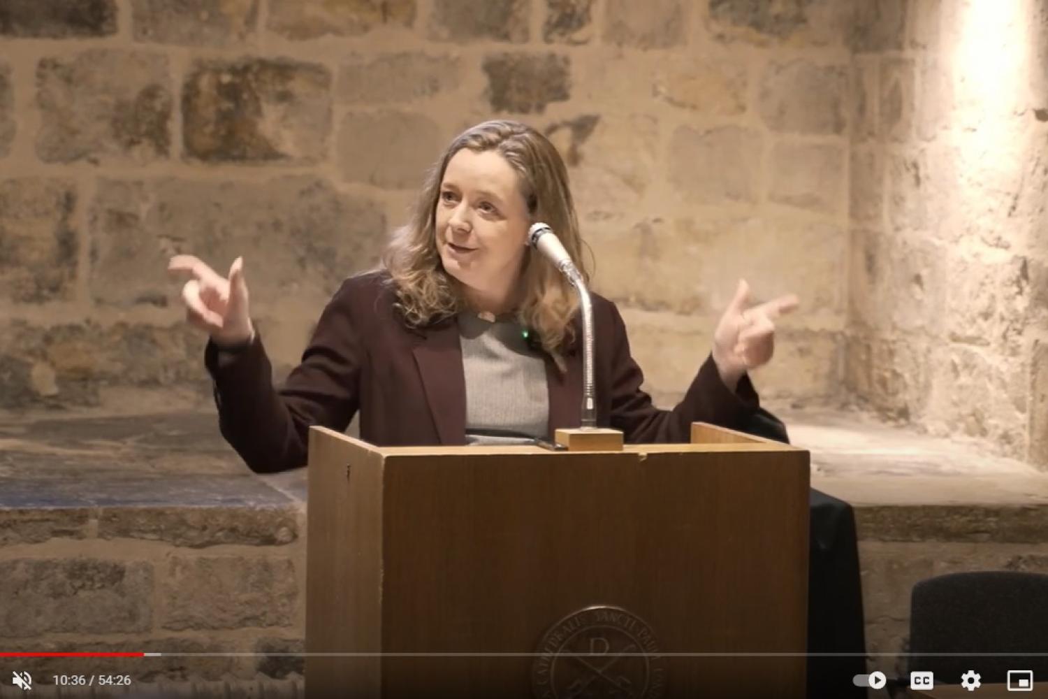 Paula Gooder, a white woman with long blond hair, talking at a lectern in the Wren Suite of St Paul's Cathedral