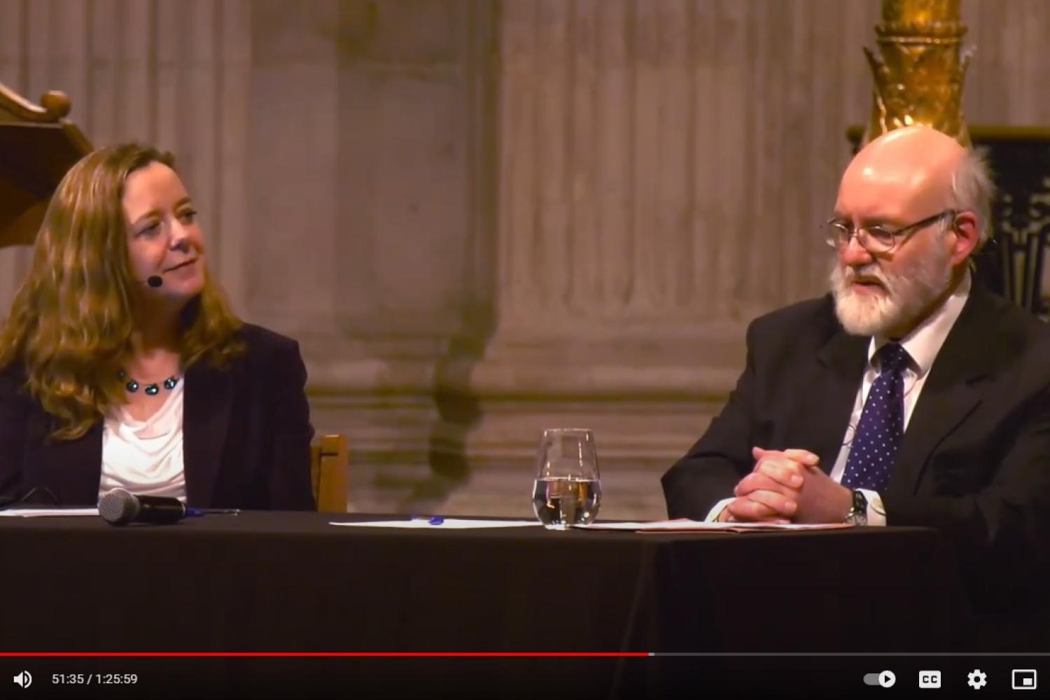 Paula Gooder and John Barton sit at a table in front of the dais at St Paul's Cathedral. John is talking and Paula smiling as she listens to him.