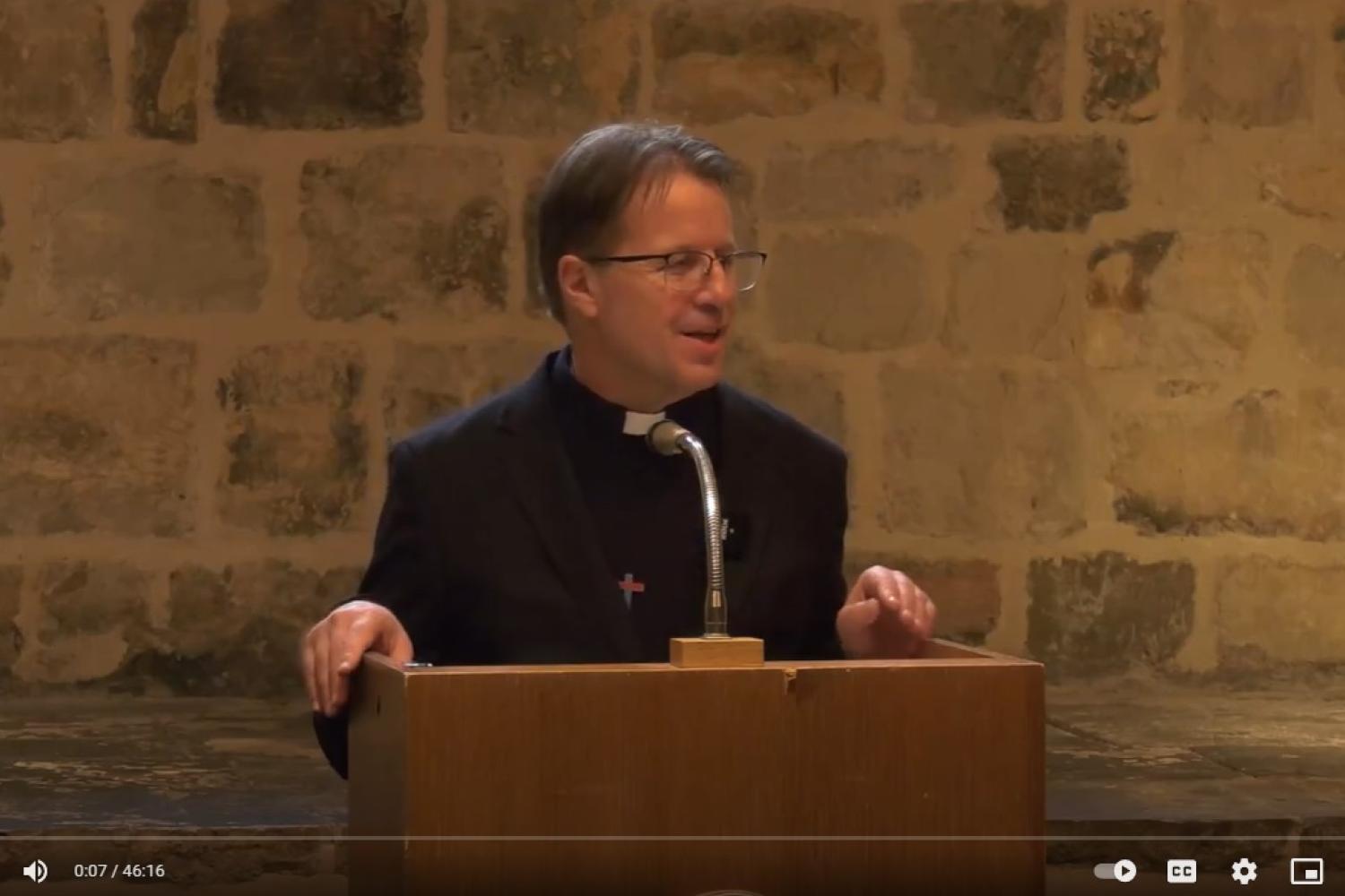 Richard Carter talks from the lectern in the Wren Suite at St Paul's, an exposed brick wall behind him.