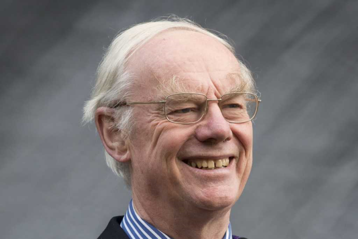 A grey-haired white man with glasses wearing academic robes over a suit and tie.