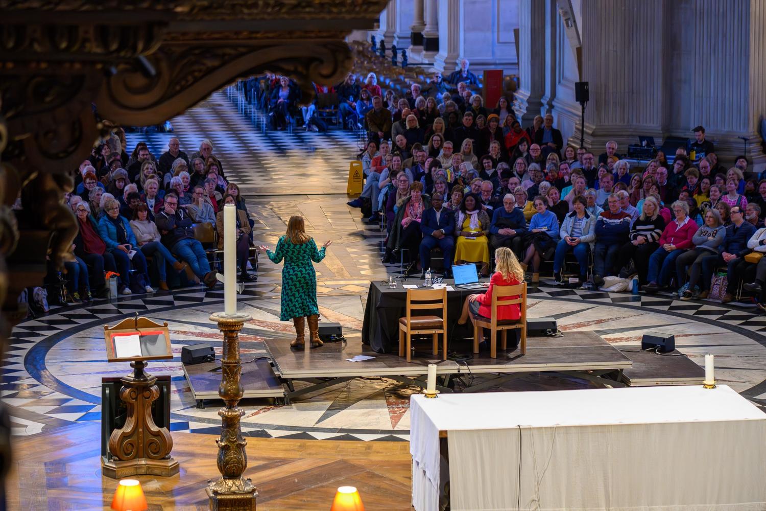 A view of the cathedral with a large audience facing a stage with a speaker in a green dress
