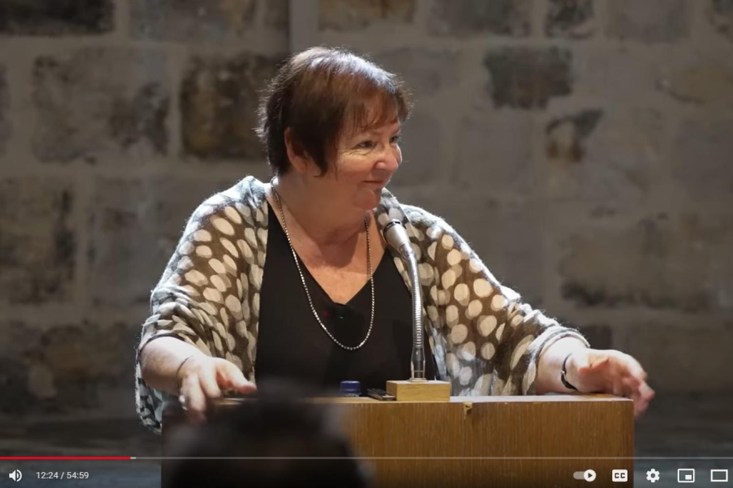 Michelle is a white woman with short auburn hair speaking at a lectern in the Wren Suite at St Paul's