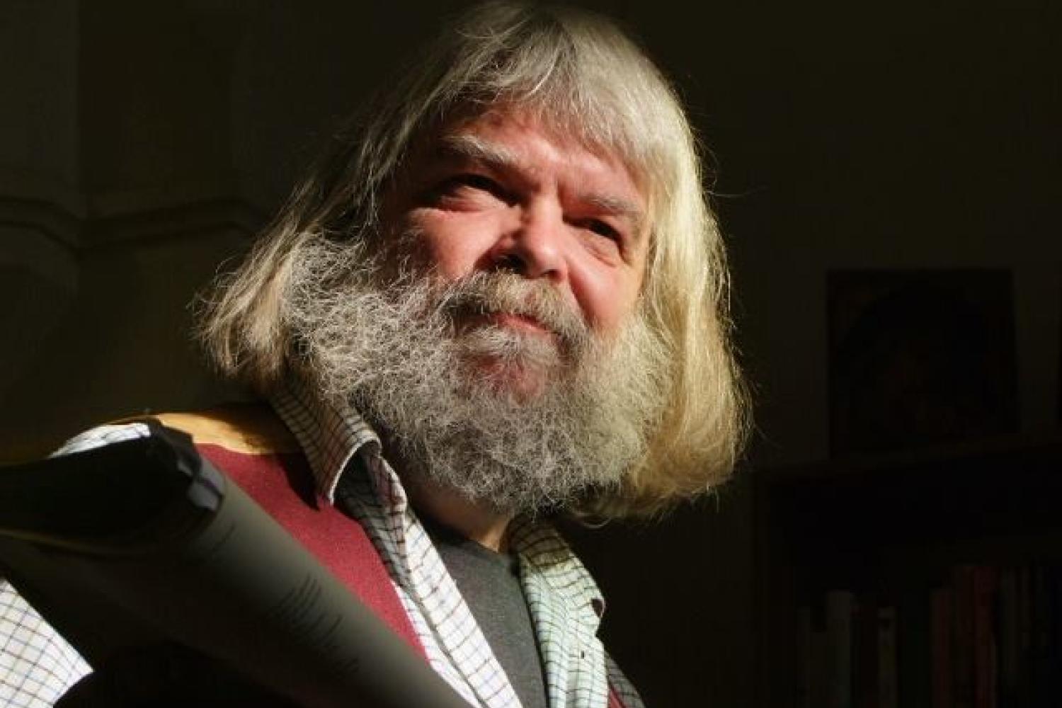 Malcolm is a white man with longish grey hair and a full beard