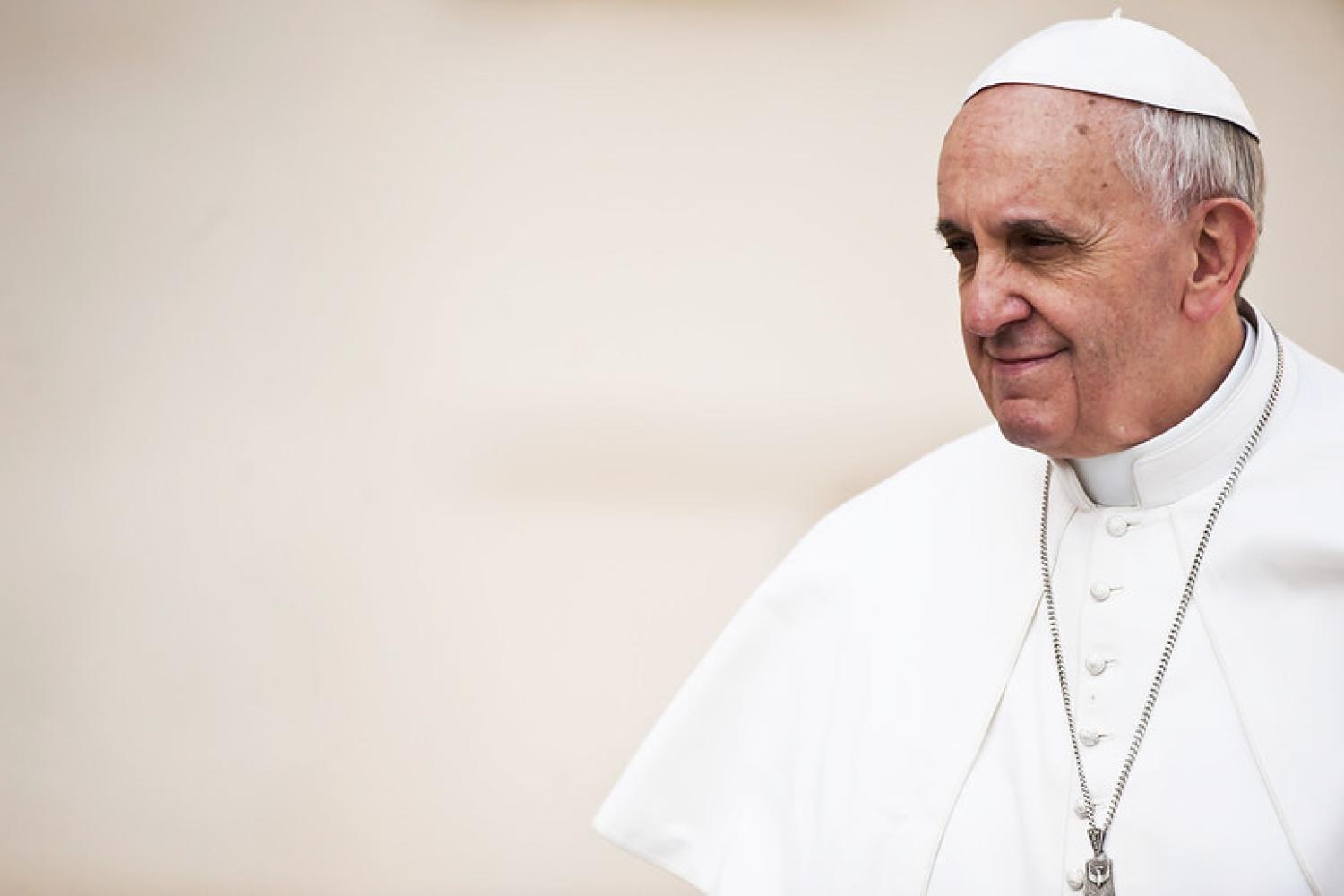 Pope Francis stands against a pale background