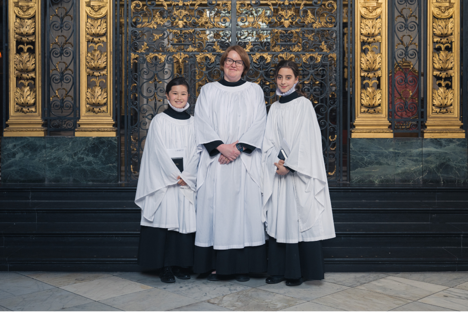 Two girl choristers pose in front of the Dean's Aisle with Carris Jones, Girls' Voices Project Manager.
