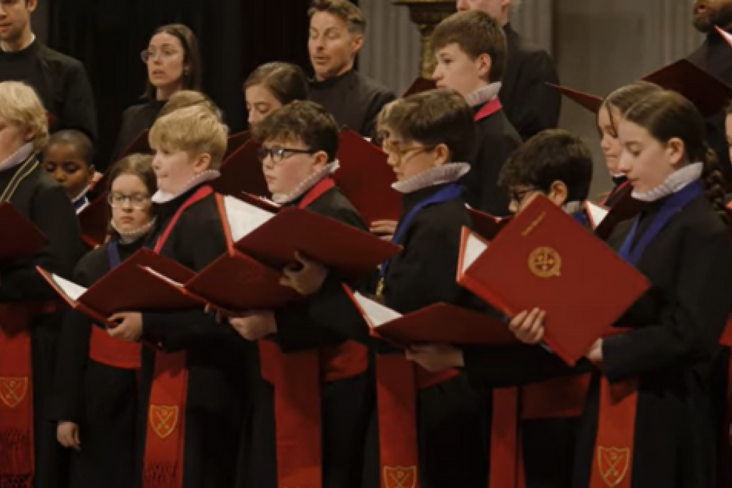 Choir in black and red robes singing holding red and black books
