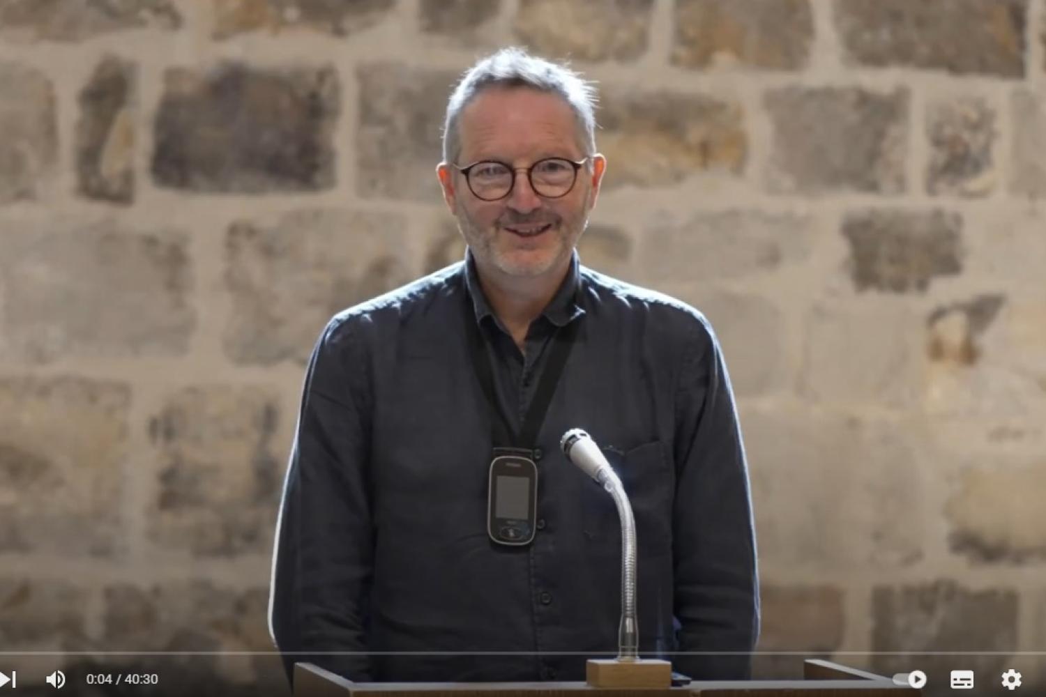 Martin stands at a microphone in the Wren Suite
