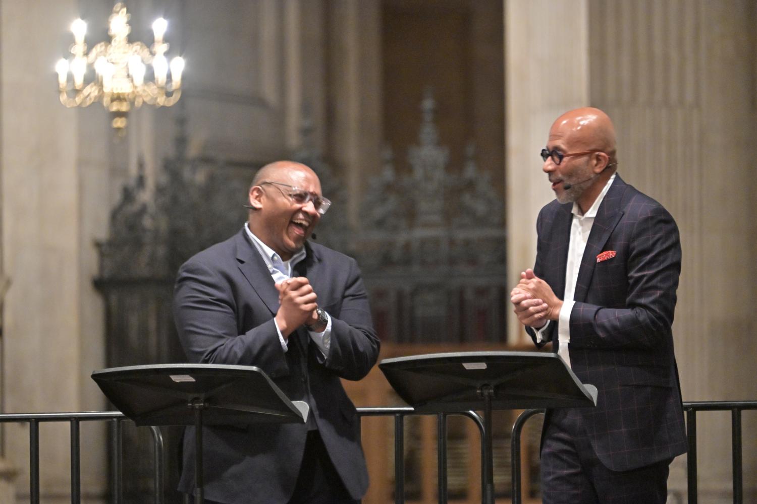 Two black men are standing on a stage in the Cathedral and laughing as they converse