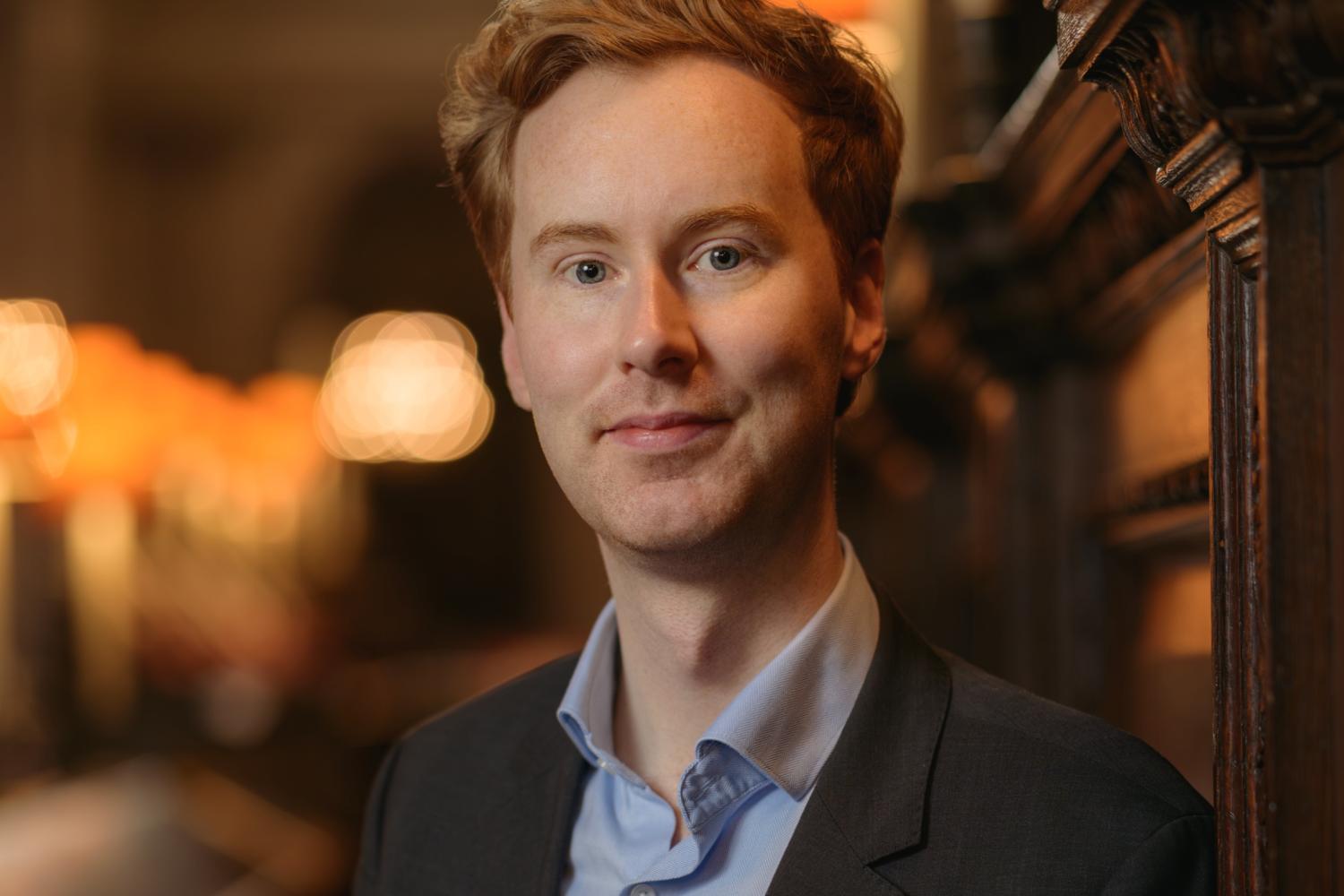 James stands in the quire of St Paul's Cathedral wearing a black jacket over a pale blue shirt
