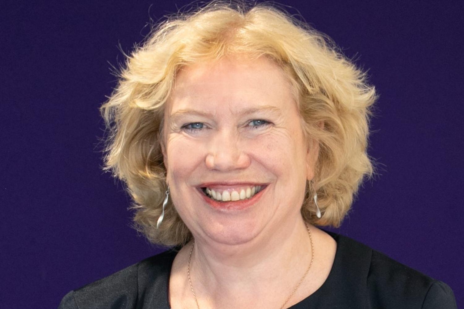 Meg Munn, a white woman with blonde hair, photographed in front of a navy blue background.