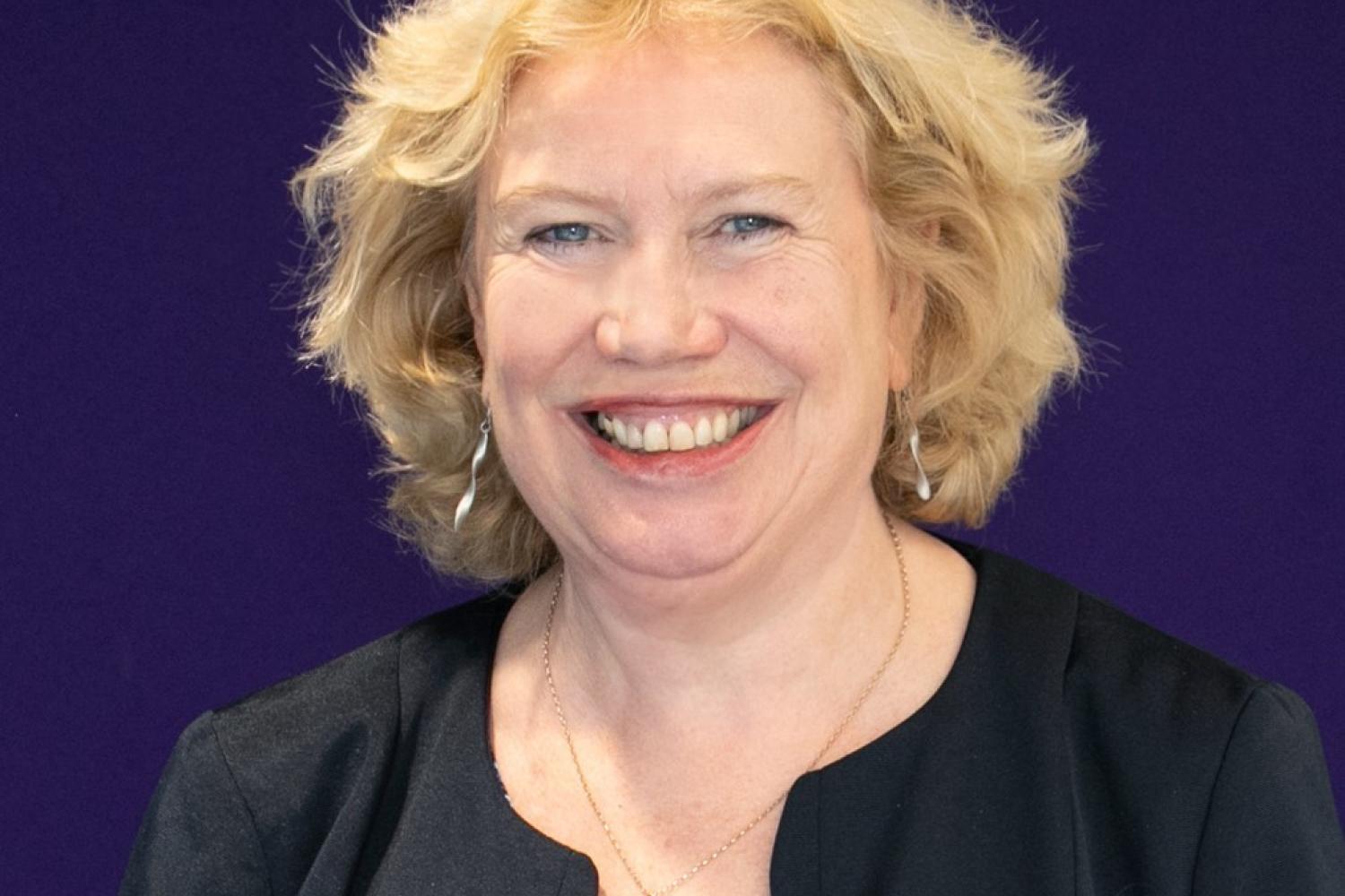 Meg Munn, a white woman with blonde hair, photographed in front of a navy blue background.
